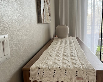 Może przedstawiać: Biały, szydełkowy bieżnik stołowy z frędzlami i małą etykietą z napisem "Handmade by Lori". Bieżnik leży na drewnianym stole.