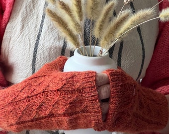 Puede incluir: Un par de guantes sin dedos de punto naranja con un jarrón de cerámica blanco lleno de hierbas secas beige.