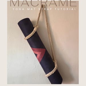 Puede incluir: Una esterilla de yoga enrollada con un diseño geométrico en rojo y burdeos, asegurada por una correa de macramé beige. La imagen presenta el texto "MACRAME YOGA MAT STRAP TUTORIAL". La esterilla cuelga contra una pared neutra.