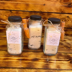 May include: Three glass jars with lids and wooden spoons filled with bath salts. The jars have labels that say "Crescent Moon Treasures" and "Pixie Bee" with a floral design.