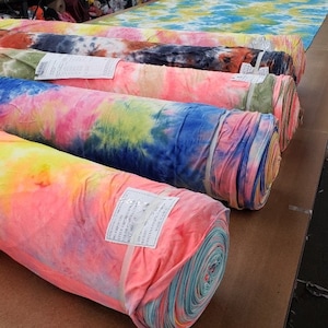 Könnte beinhalten: Fünf Rollen mit Batik-Stoff in verschiedenen Farben, darunter Pink, Gelb, Blau und Grün. Der Stoff ist aufgerollt und übereinander gestapelt.