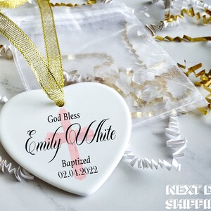 Pu&ograve; includere: Un ornamento bianco a forma di cuore con nastro dorato, con la scritta "God Bless Emily White Baptized 02.04.2022" e una croce rosa. L'ornamento &egrave; confezionato con imbottitura decorativa bianca e oro.