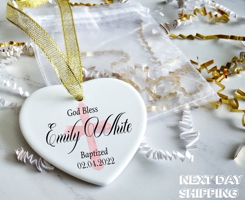 Pu&ograve; includere: Un ornamento bianco a forma di cuore con nastro dorato, con la scritta "God Bless Emily White Baptized 02.04.2022" e una croce rosa. L'ornamento &egrave; confezionato con imbottitura decorativa bianca e oro.