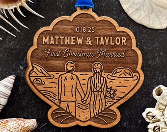 May include: A wooden Christmas ornament shaped like a seashell with a couple standing on a beach. The ornament is engraved with the text "10.18.25 Matthew & Taylor First Christmas Married".
