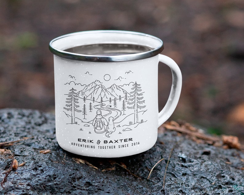 May include: White enamel camping mug with a black line drawing of a couple and a dog hiking in the mountains. The mug has the text "Erik & Baxter Adventuring Together Since 2014" printed on the bottom.