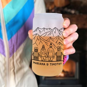 May include: A frosted glass can with a mountain scene and two skiers holding hands. The text "MARIANA & TIMOTHY" is printed at the bottom of the can.