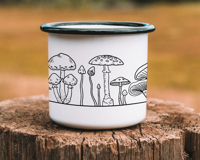 May include: White enamel mug with a black outline of various mushrooms. The mug has a black rim and handle.