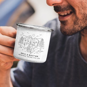 May include: White enamel camping mug with a black and white illustration of a couple hiking in the mountains. The mug has the text "Erik & Baxter Adventuring Together Since 2014" printed on it.