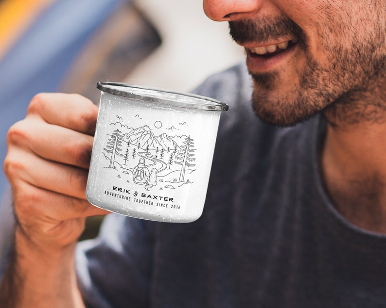 May include: White enamel camping mug with a black and white illustration of a couple hiking in the mountains. The mug has the text "Erik & Baxter Adventuring Together Since 2014" printed on it.