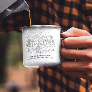 May include: A white enamel camping mug with a black line drawing of a person and a dog hiking in the mountains. The mug has the text "Erik & Baxter Adventuring Together Since 2014" printed on the bottom.