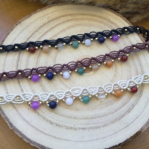 Può includere: Tre cavigliere con cordini di diversi colori e perline di pietre preziose. Le cavigliere sono realizzate con un motivo a nodo macramé. Le perline sono in tonalità di viola, verde, arancione, rosso e blu.