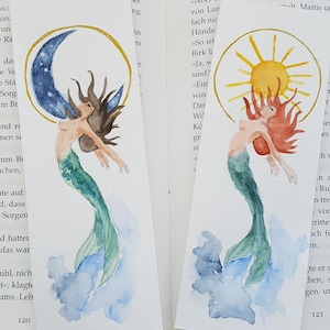 Op de afbeelding: Twee aquarel illustraties van zeemeerminnen. De eerste zeemeermin heeft bruin haar en een blauwe halve maan boven haar. De tweede zeemeermin heeft rood haar en een gele zon boven haar. Beide zeemeerminnen hebben groene staarten en zwemmen in blauw water.