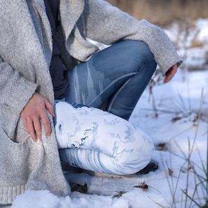 May include: A person wearing a gray cardigan and white and blue patterned leggings. The person is kneeling in the snow.