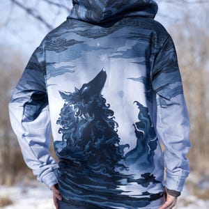 May include: A blue and white hooded sweatshirt featuring a wolf howling at the moon graphic. The wolf is surrounded by clouds and stars.