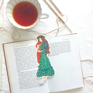 Pu&ograve; includere: Un segnalibro con una donna in un vestito floreale verde che abbraccia una volpe, posto su un libro aperto. Una tazza di t&egrave; e ferri da maglia sono sullo sfondo. Il libro &egrave; intitolato "The Wind in the Willows".