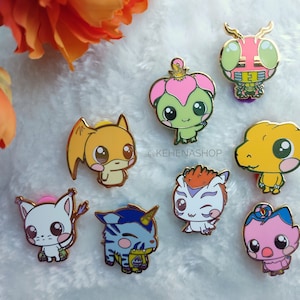 May include: A set of eight gold-colored enamel pins featuring various cartoon characters. The characters include a pink and green creature with a crown, a yellow creature with a red heart, a white creature with a red bow, a blue and yellow creature with a horn, a yellow creature with a red heart, a white creature with a red bow, a yellow creature with a red heart, and a pink and green creature with a crown. The pins are all about 1 inch in diameter.