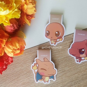 Könnte beinhalten: Drei bunte Comic-Charakter-Lesezeichen mit Pokemon-Charakteren. Die Lesezeichen sind auf weißem Hintergrund mit rosa Rand gedruckt. Die Charaktere sind Charmander, Bulbasaur und Squirtle.