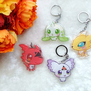 Peut inclure: Quatre porte-clés de personnages d'anime colorés avec des anneaux de clés argentés. Les personnages sont un dragon rouge, une créature verte et blanche, un renard jaune et une créature violette et blanche.