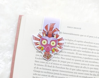 Op de afbeelding: Een bladwijzer met een cartoonillustratie van Majora's Mask uit de The Legend of Zelda-videogameserie. Het masker is rood, geel en zwart met grote, witte ogen. De bladwijzer is gedrukt op een lichtpaarse achtergrond.