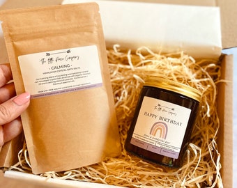 May include: A gift box filled with brown packing peanuts, a brown paper bag with the text "The Life Peace Company CALMING. HIMALAYAN CRYSTAL BATH SALTS" and a brown glass candle with a gold lid and the text "The Life Peace Company HAPPY BIRTHDAY Have a wonderful day!"