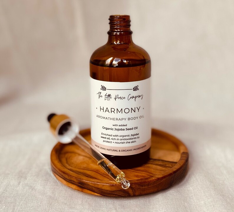 May include: A brown glass bottle with a dropper, labeled "The Little Peace Company. HARMONY. AROMATHERAPY BODY OIL with added Organic Jojoba Seed Oil. Enriched with organic Jojoba seed oil, rich in antioxidants to protect + nourish the skin. MADE USING NATURAL & ORGANIC INGREDIENTS."