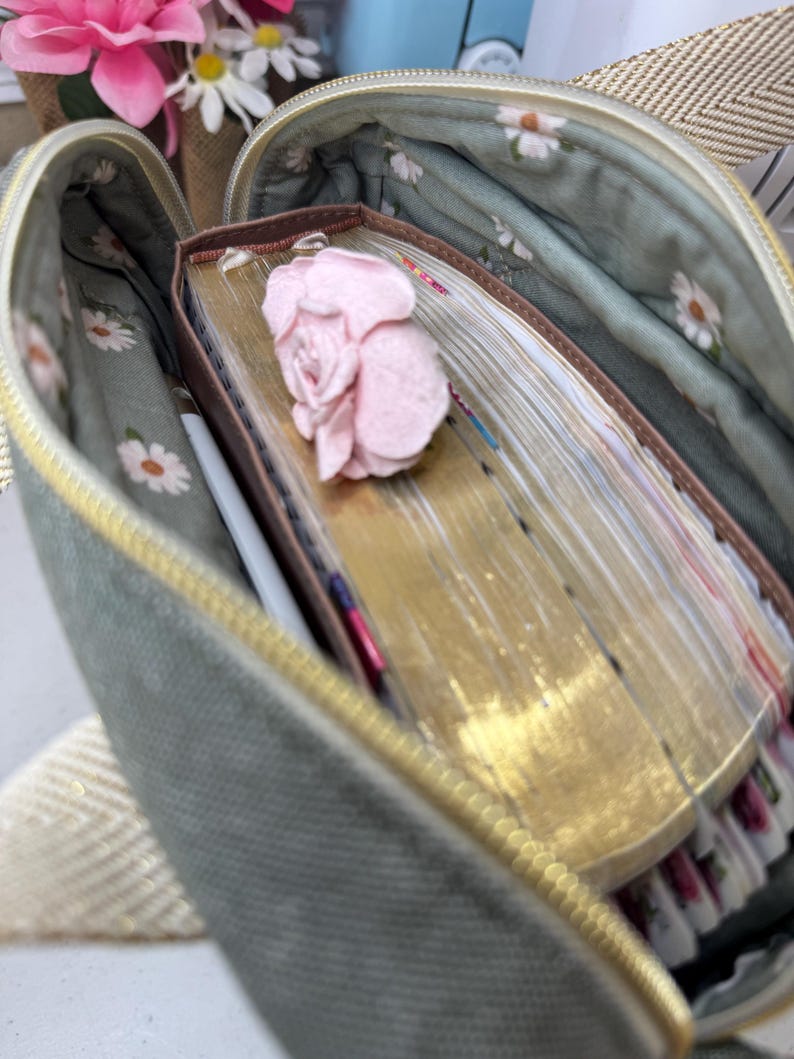 Puede incluir: Una bolsa verde con cremallera y forro floral. La bolsa est&aacute; abierta y contiene una pila de libros viejos y amarillentos con una flor rosa en la parte superior.
