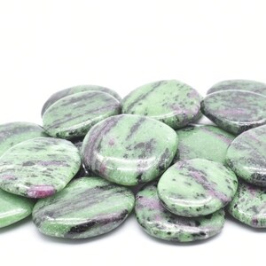 Könnte beinhalten: Eine Sammlung von grünen, schwarzen und rosafarbenen Zultanit-Trommelsteinen. Die Steine sind glatt und poliert und haben verschiedene Formen und Größen.