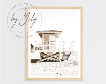 Puede incluir: Una fotografía en sepia de una caseta de salvavidas en una playa. La caseta es de madera y tiene una escalera que lleva hasta la cima. La playa está vacía y la arena es blanca.