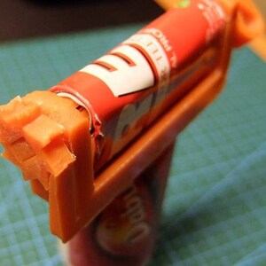 May include: An orange plastic candy cutter holding a partially unwrapped red and white candy roll. The candy has been cut into a star shape. The candy roll has the words "PRO" and "TEE" visible.