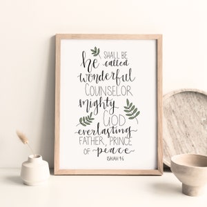 Può includere: Una stampa incorniciata con sfondo bianco e testo in calligrafia nera che recita "Egli sarà chiamato consigliere meraviglioso, Dio potente, Padre eterno, Principe della pace" con illustrazioni di foglie verdi e il testo "Isaia 9:6" in basso.