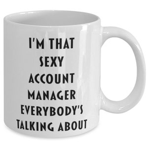 May include: White ceramic coffee mug with black text that reads "I'm that sexy account manager everybody's talking about".