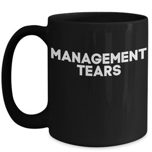 May include: Black ceramic coffee mug with white text that reads "MANAGEMENT TEARS".