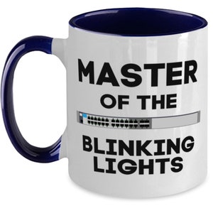 May include: White ceramic mug with a navy blue interior and handle. The mug features the text "MASTER OF THE BLINKING LIGHTS" in black, with a graphic of a network switch.