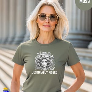 Puede incluir: Una camiseta verde con un gráfico de una mujer con serpientes como cabello. El texto "JUSTIFIABLY PISSED" está impreso debajo del gráfico.