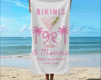 May include: White beach towel with pink text that reads "Bikinis & Martinis" and "Emily's Bachelorette Austin, Texas". A pink martini glass with green olives is pictured in the center of the towel.