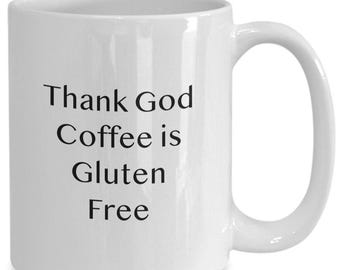May include: A white ceramic mug with a handle on the right side. The front of the mug features black printed text that reads: Thank God Coffee is Gluten Free. The mug has a smooth, glossy finish and a cylindrical shape with a standard rim and base.