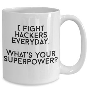 May include: A white ceramic mug featuring black text that reads I FIGHT HACKERS EVERYDAY. WHAT'S YOUR SUPERPOWER? The mug has a standard cylindrical shape with a curved handle on the right side, providing a clear view of the printed message.