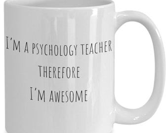 May include: A white ceramic mug with a handle on the right side. The front of the mug features black text that reads: I'M A PSYCHOLOGY TEACHER THEREFORE I'M AWESOME. The mug has a smooth, glossy finish and a cylindrical shape with a standard rim.