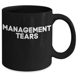 May include: Black ceramic coffee mug with white text that reads "MANAGEMENT TEARS".