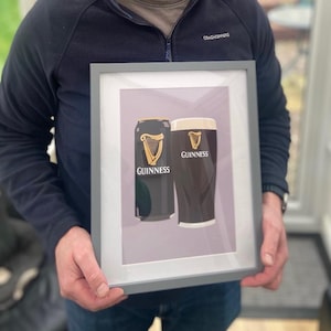 Peut inclure: Impression encadr&eacute;e repr&eacute;sentant une canette et un verre de Guinness. La canette est noire avec un logo de harpe dor&eacute;e et le mot "Guinness". Le verre est sombre avec une t&ecirc;te cr&eacute;meuse, portant &eacute;galement le logo Guinness.