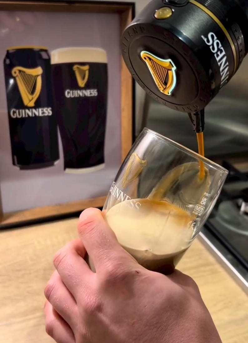 Peut inclure: Verre de Guinness en cours de remplissage. La bi&egrave;re brune coule d'un robinet dans un verre inclin&eacute;. En arri&egrave;re-plan, une image encadr&eacute;e d'une canette et d'un verre de Guinness. Le logo Guinness est visible.