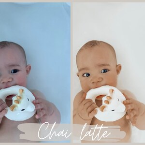 May include: A baby in a white bathtub is holding a white and gold bath toy shaped like a unicorn. The baby is biting the toy and looking at the camera. The text "Chai latte" is written on the bottom of the image.