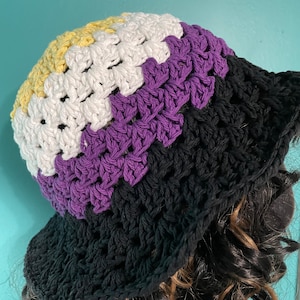 May include: A crocheted bucket hat with a yellow, white, purple, and black color scheme. The hat is made with a simple stitch pattern and has a wide brim.