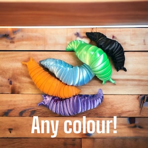 Op de afbeelding: Vijf kleurrijke, pluche, wormvormige speelgoedjes. De wormen zijn in een stapel gerangschikt, met de groene worm bovenop. De wormen zijn gemaakt van zacht, pluche stof en hebben een verscheidenheid aan kleuren, waaronder groen, blauw, oranje, paars en zwart.