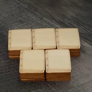 May include: Five stacks of square wooden tiles with a light beige surface and a decorative border. The edges of the tiles are a darker brown. The tiles are arranged on a dark grey wooden surface.