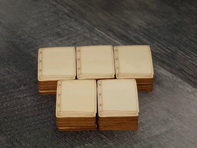 May include: Five stacks of square wooden tiles with a light beige surface and a decorative border. The edges of the tiles are a darker brown. The tiles are arranged on a dark grey wooden surface.