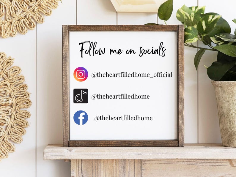 May include: A wooden framed sign with the words "Follow me on socials" in black script. Below the text are the Instagram, TikTok, and Facebook logos with usernames. The sign is displayed on a wooden shelf.