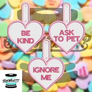 Könnte beinhalten: Drei rosa herzförmige Etiketten mit weißem Hintergrund und rosa Rändern. Die Etiketten tragen folgenden Text: "Be Kind", "Ask to Pet" und "Ignore Me".
