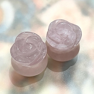 Puede incluir: Dos tapones de cuarzo rosa, tallados en forma de rosas. Los tapones son de color rosa suave y tienen tallas detalladas de pétalos. El fondo es una superficie clara y multicolor. Estos tapones son un accesorio único.
