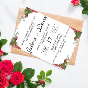 May include: Wedding invitation featuring the names "Juliana & Daniel" in elegant script. The white card is adorned with floral accents and the date "JUN 17 2050". The invitation is placed on a brown envelope, surrounded by red roses.